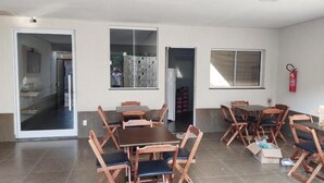 A dining area with wooden tables and chairs, a fire extinguisher on the wall, and a sliding glass door leading to a corridor. - Hotel Habitar (Serra do Salitre)