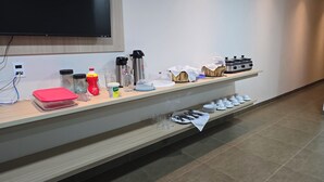 A hotel reception area with a wooden counter displaying various amenities including a TV, bottled water, a coffee maker, and a food display. - Hotel Habitar (Serra do Salitre)