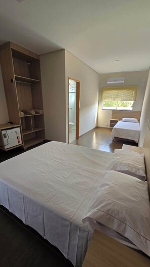 A bedroom with two beds, a wardrobe, a small table, and a window with blinds. - Hotel Habitar (Serra do Salitre)