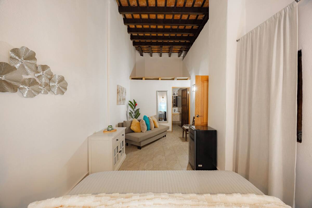 A bedroom with a bed, a dresser, a mirror, a sofa, and a plant.