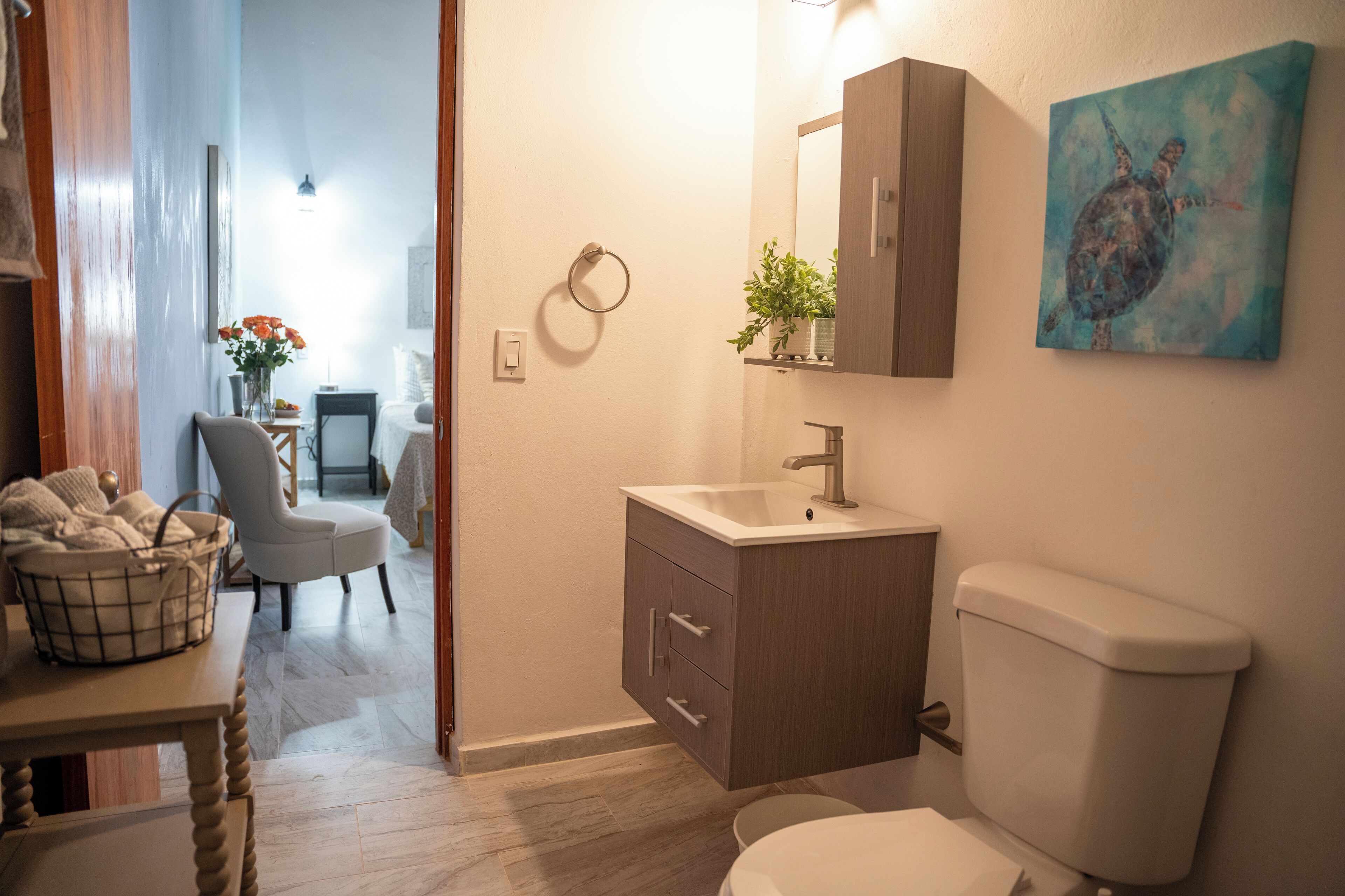 A bathroom with a toilet, sink, cabinet, and a painting on the wall.