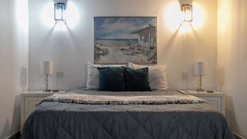 Une chambre à coucher avec un lit, deux lampes de chevet, un tableau représentant une scène de plage et une table de chevet avec une lampe.