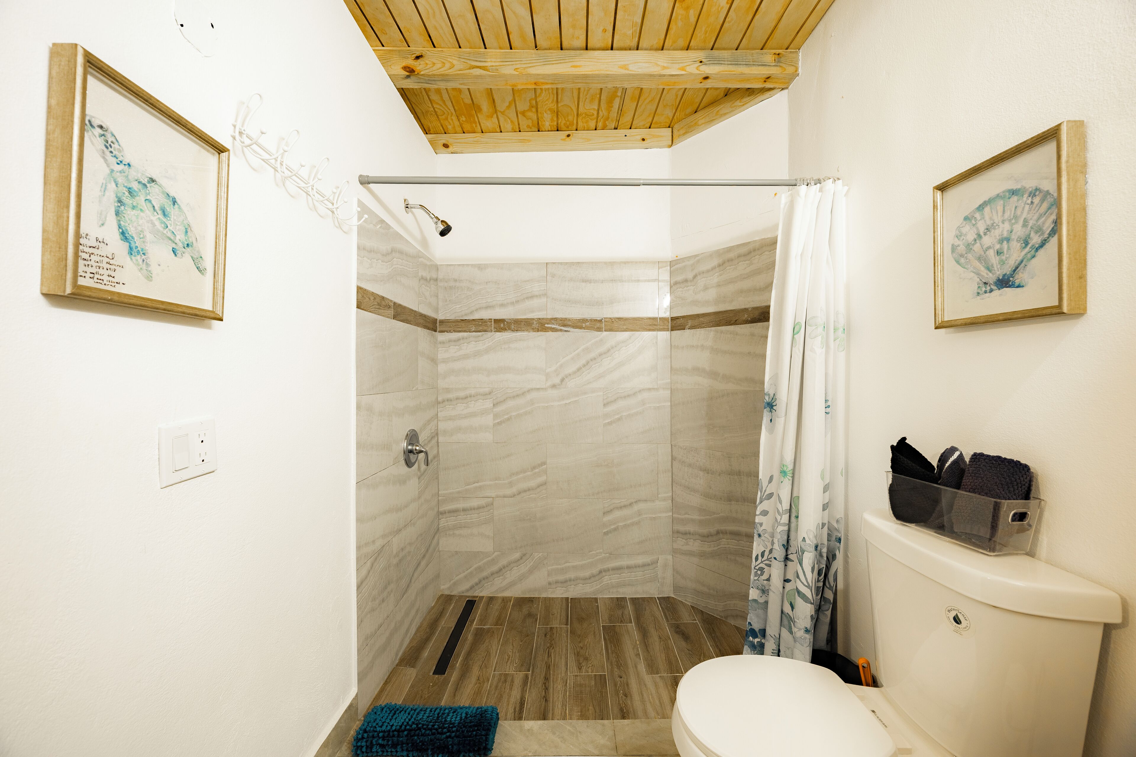 A bathroom with a shower, toilet, and two framed pictures on the walls.