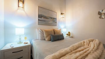 A neatly arranged bedroom with a bed, bedside tables, lamps, and a painting on the wall.