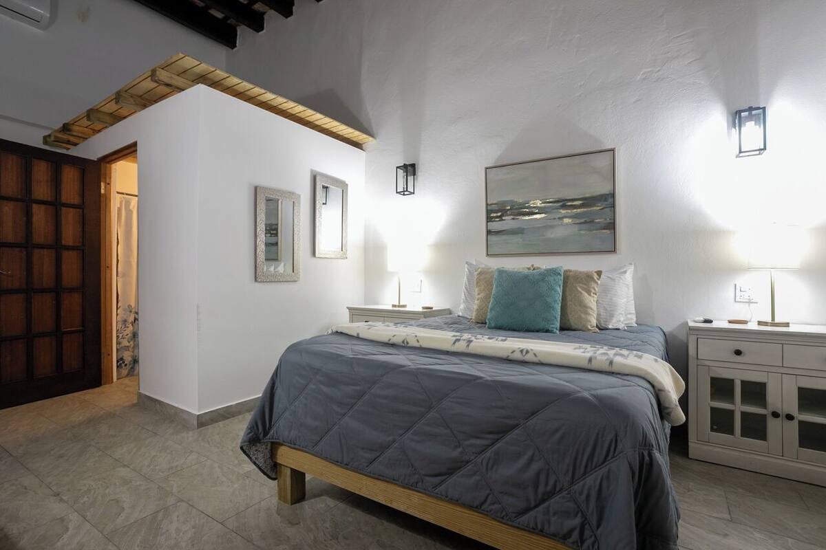 A bedroom with a bed, bedside tables, a nightstand, a wooden door, and a painting on the wall.