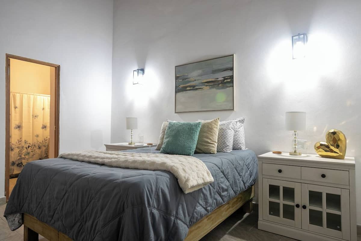 A bedroom with a bed, bedside tables, a nightstand, a cabinet, a painting, and a window.