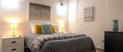 Un dormitorio con una cama, dos mesitas de noche con lámparas, un tocador y luces en la pared.
