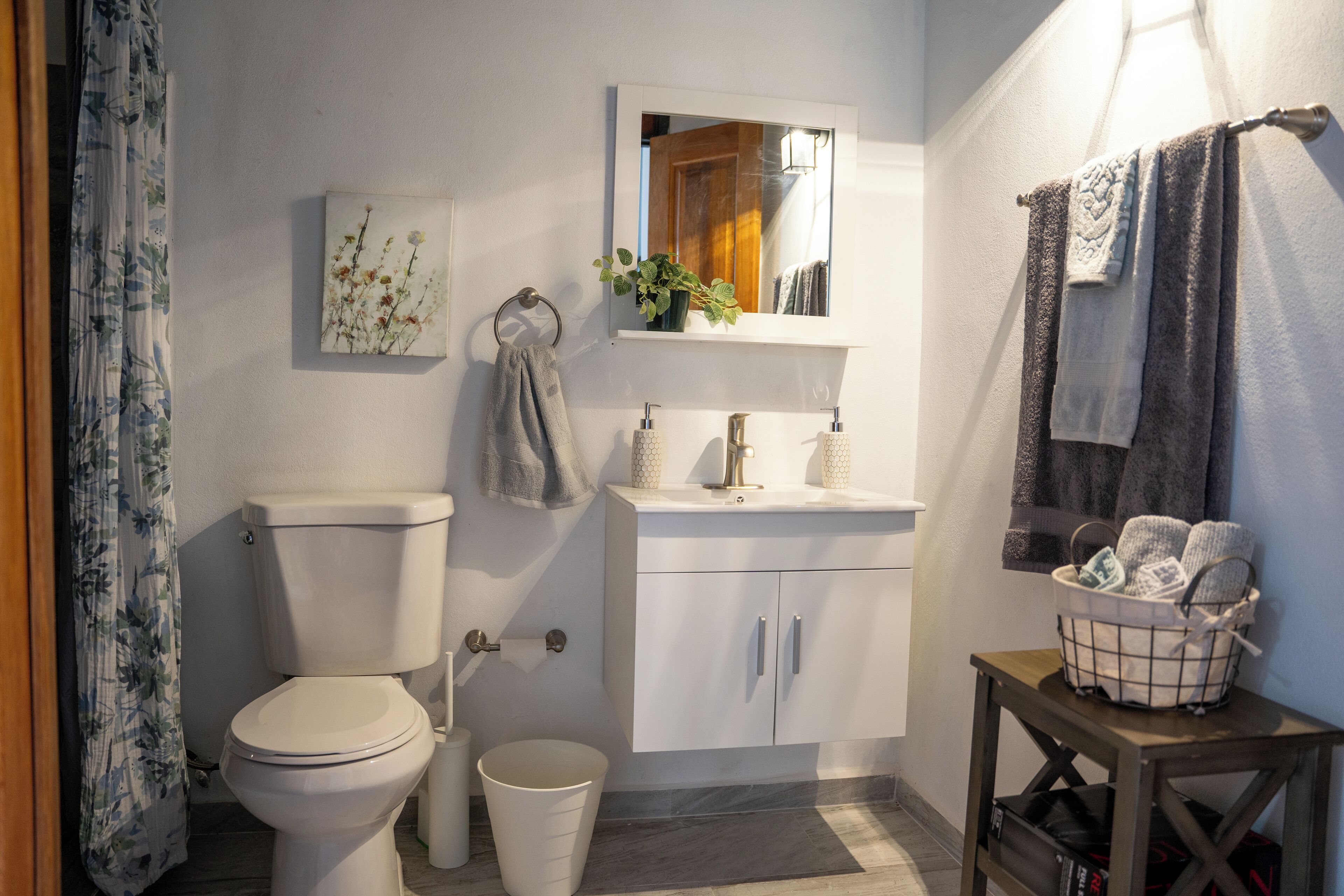 A bathroom with a toilet, sink, mirror, and a small table with a basket.