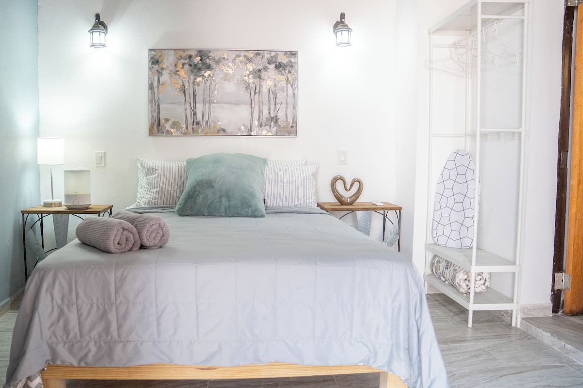 A bedroom with a bed, bedside tables, a nightstand, a wall-mounted lamp, a painting, and a wardrobe.