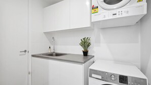 Una cocina pequeña con un lavamanos, una planta en maceta y una lavadora blanca.