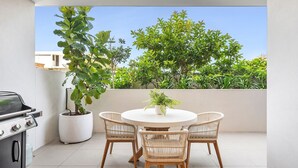 Un patio al aire libre con una mesa redonda y cuatro sillas de mimbre, una parrilla y una planta en maceta.