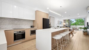 Una cocina moderna con armarios blancos, una isla grande con taburetes, electrodomésticos integrados y vistas al exterior.