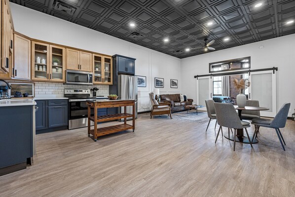Una cocina moderna con armarios de madera, microondas integrado y comedor con sillas grises y una mesa redonda.