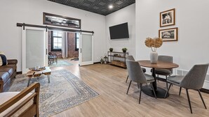 Amplia sala de estar con una gran mesa de comedor de madera, sillas tapizadas de color gris, una mesa de centro y un tapete estampado.
