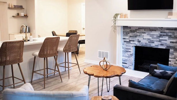 Una sala de estar moderna con chimenea, un comedor con taburetes de bar y una cocina con barra para café.