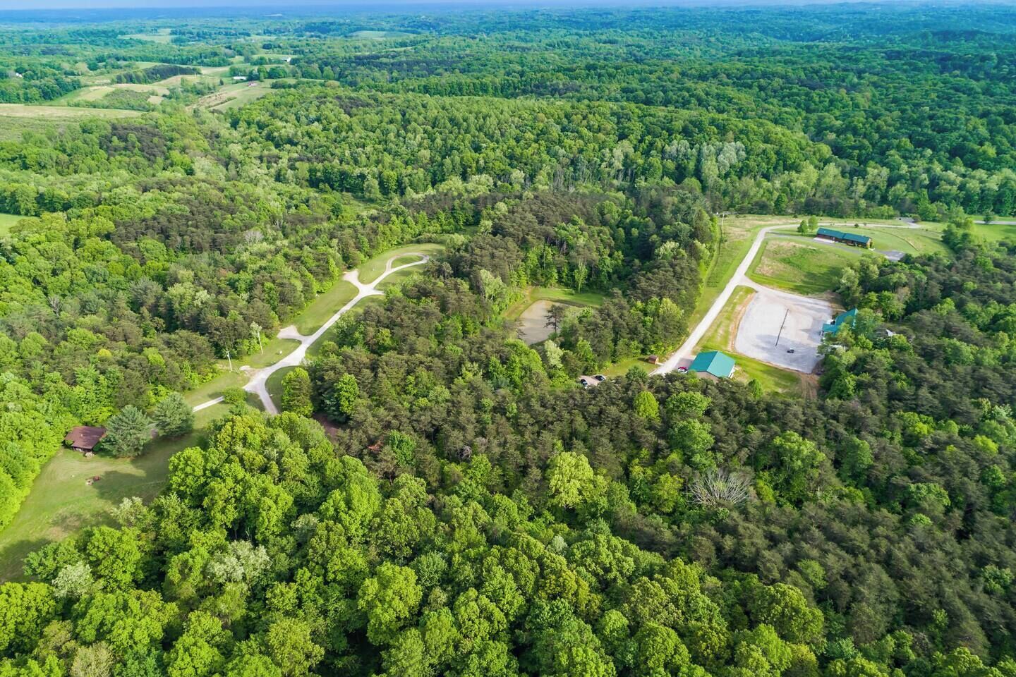 Vista aérea de un área boscosa con un camino despejado, un edificio pequeño y un estacionamiento.