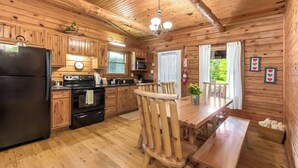 A wooden cabin kitchen with a refrigerator, stove, microwave, wooden cabinets, and a dining table with chairs.