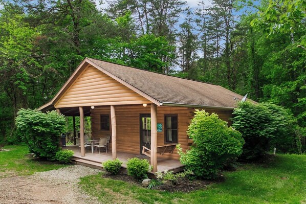 Uma cabana de tronco com varanda, área de refeições e um pequeno jardim.