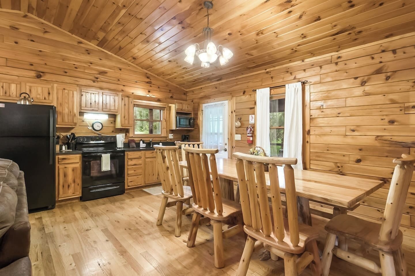 Interior de una cabaña de madera con cocina, comedor y un amplio ventanal.