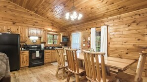 Interior de una cabaña de madera con cocina, comedor y un amplio ventanal.