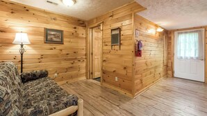 Una habitación con paneles de madera, un sofá, una lámpara, un cuadro enmarco, una puerta y un extintor.