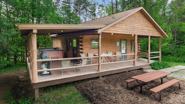 Una cabaña de troncos con un porche cubierto, mobiliario exterior y una zona de barbacoa.