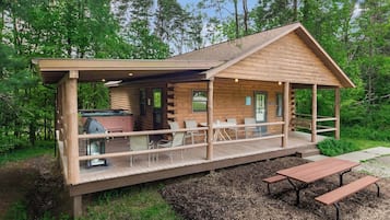 Una cabaña de troncos con un porche cubierto, mobiliario exterior y una zona de barbacoa.