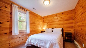 Un dormitorio con paneles de madera, una cama, una ventana con cortinas, una mesita de noche y una lámpara.