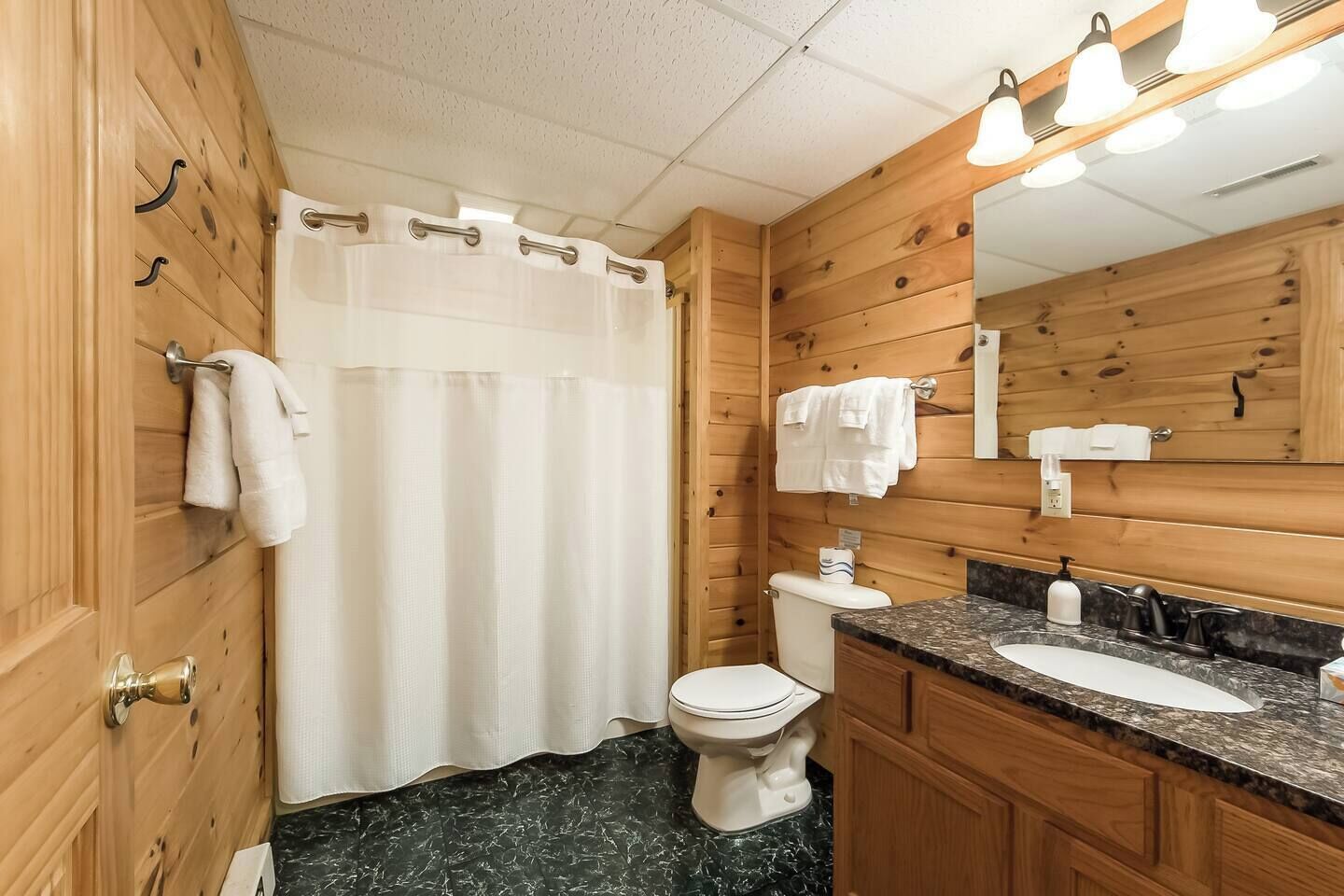 Een betegelde badkamer met douchegordijn, toilet, wastafel en spiegel.