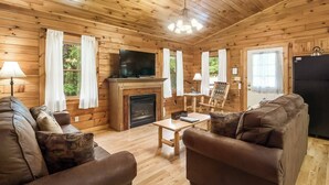 Un acogedor interior de cabaña con chimenea, paredes de madera, un televisor y sofás de cuero.
