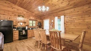A wooden cabin kitchen with a black refrigerator, stove, microwave, and wooden chairs around a table. - Family & Friends Getaway |Near Old Man's Cave (Logan)