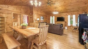 A wooden cabin interior with a dining table, chairs, a sofa, a television, and a refrigerator. - Family & Friends Getaway |Near Old Man's Cave (Logan)