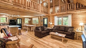 Uma cabana espaçosa com área de refeições, cozinha e uma ampla sala de estar com sofá e televisão.
