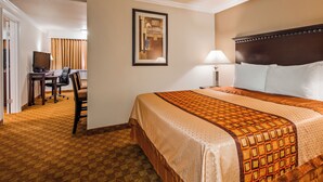 A hotel room with a large bed, a desk with a chair, a lamp, and a framed picture on the wall.