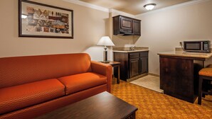 A compact living space with a sofa, a small table, a lamp, a kitchenette with a microwave, and a framed picture on the wall.