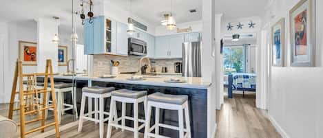 A modern kitchen with a central island, bar stools, and pendant lighting.