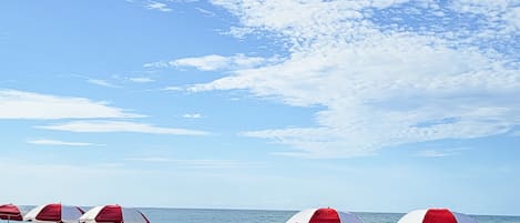 A beach with rows of red and white beach chairs and umbrellas, a sandy shore, and the ocean in the background.
