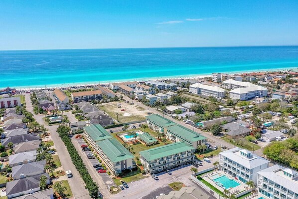 A coastal hotel with multiple buildings, a parking lot, and a pool area.