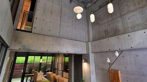 Un intérieur moderne avec des murs en béton, des luminaires suspendus et un espace salon bien délimité, avec des tables et des chaises.