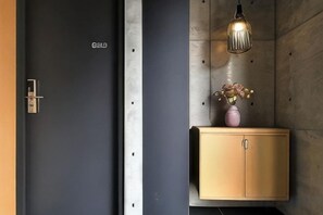Une porte sombre avec un trou de serrure, un meuble en bois surmonté d’un vase et un luminaire suspendu.