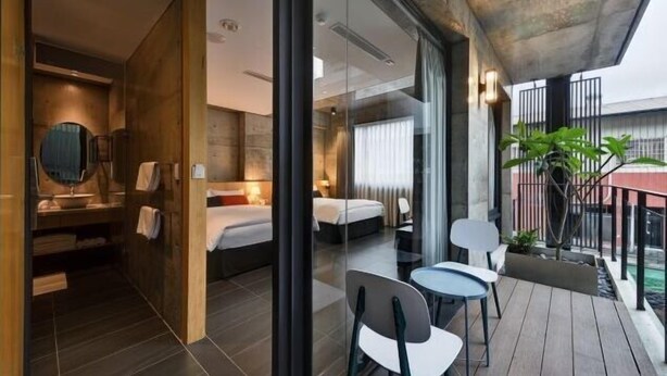Une chambre d’hôtel moderne dotée d’un balcon, d’un grand lit, d’un coin salon avec des fauteuils et d’une petite table.