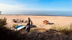 Una playa con una terraza de madera que lleva a la arena, una tabla de surf y sillas de playa.