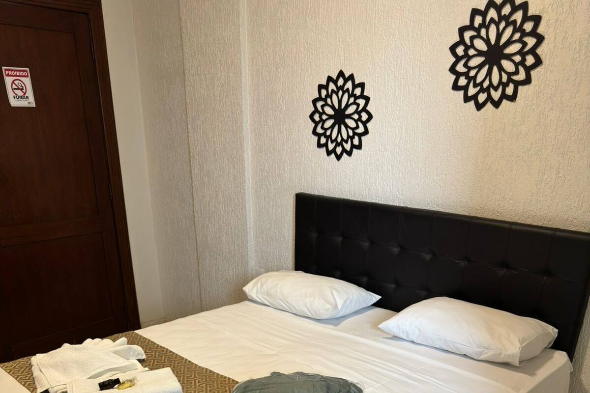 Cama bem arrumada com lençóis brancos, colcha estampada e travesseiro verde.