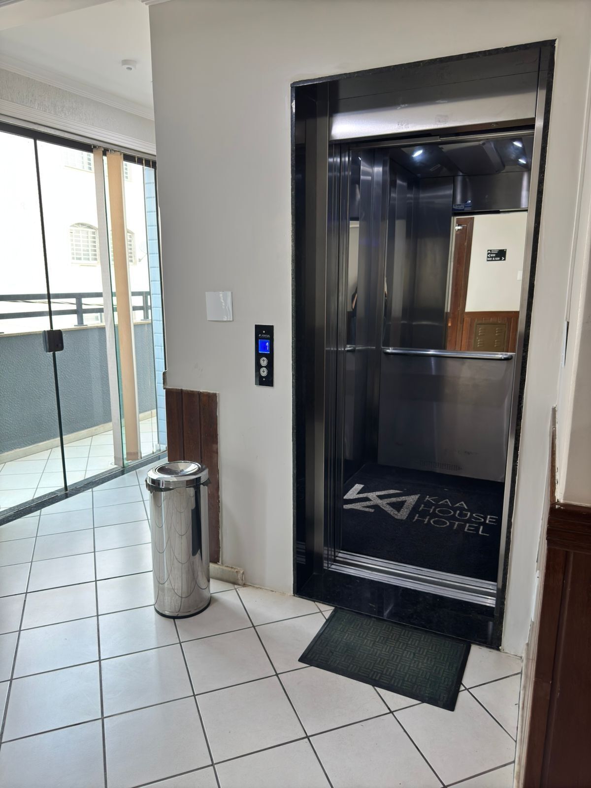 An elevator with a digital display, a trash bin, and a doormat in a hotel lobby.