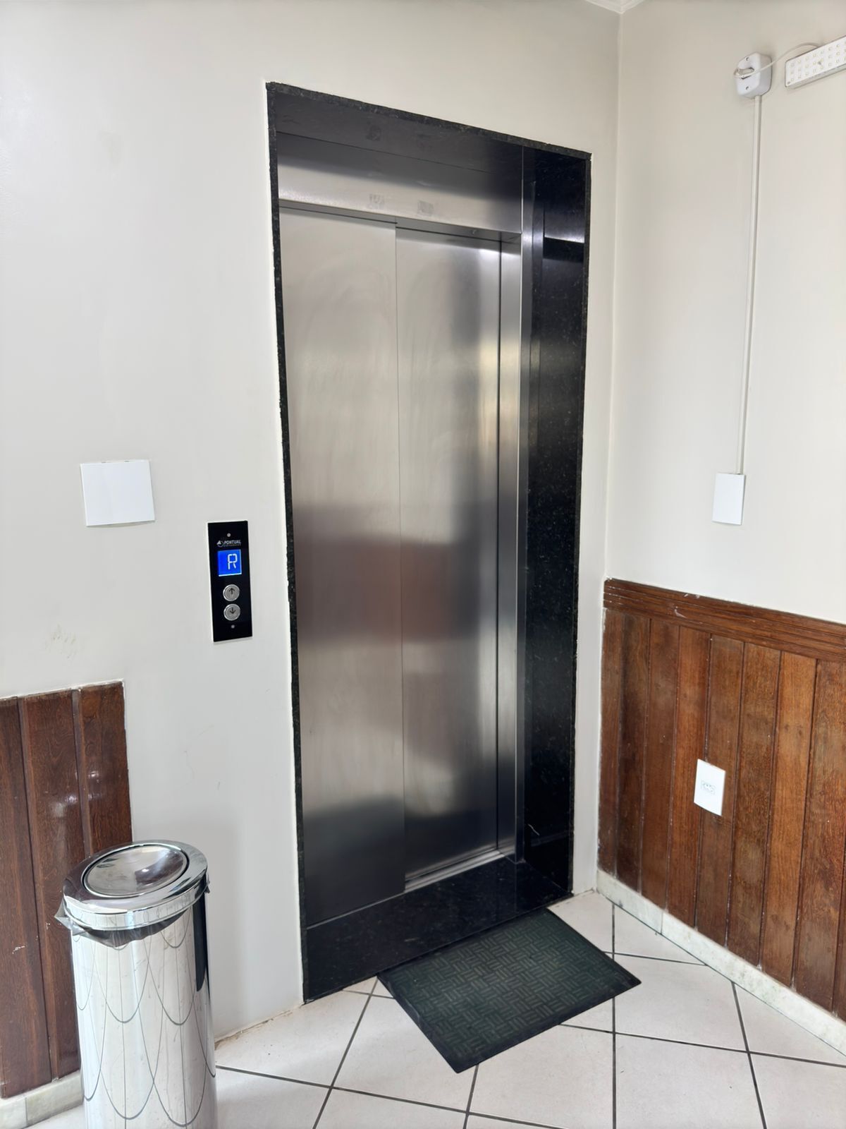 A modern elevator with a digital control panel, a trash bin, and a wooden panel wall.
