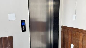 A modern elevator with a digital control panel, a trash bin, and a wooden panel wall.