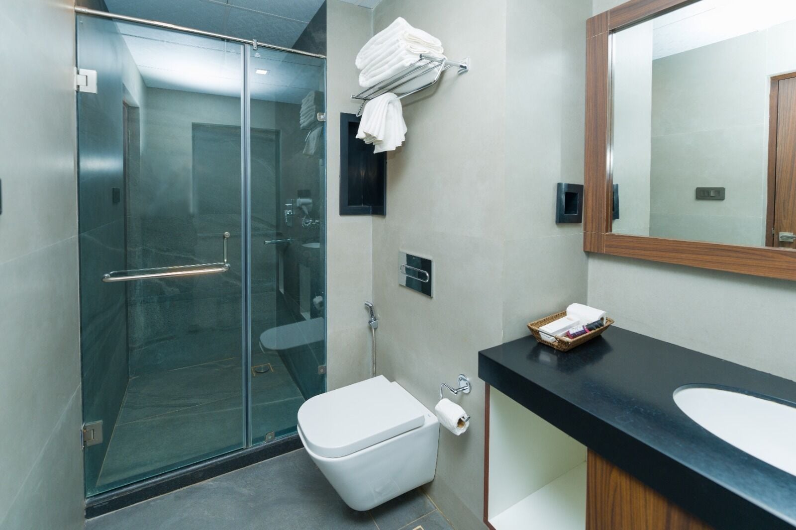 A modern bathroom with a glass shower enclosure, a white toilet, a black countertop with a sink, and a mirror.