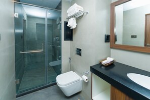 A modern bathroom with a glass shower enclosure, a white toilet, a black countertop with a sink, and a mirror. - PRUDENTIAL HOTEL NEPAL (Kathmandu)