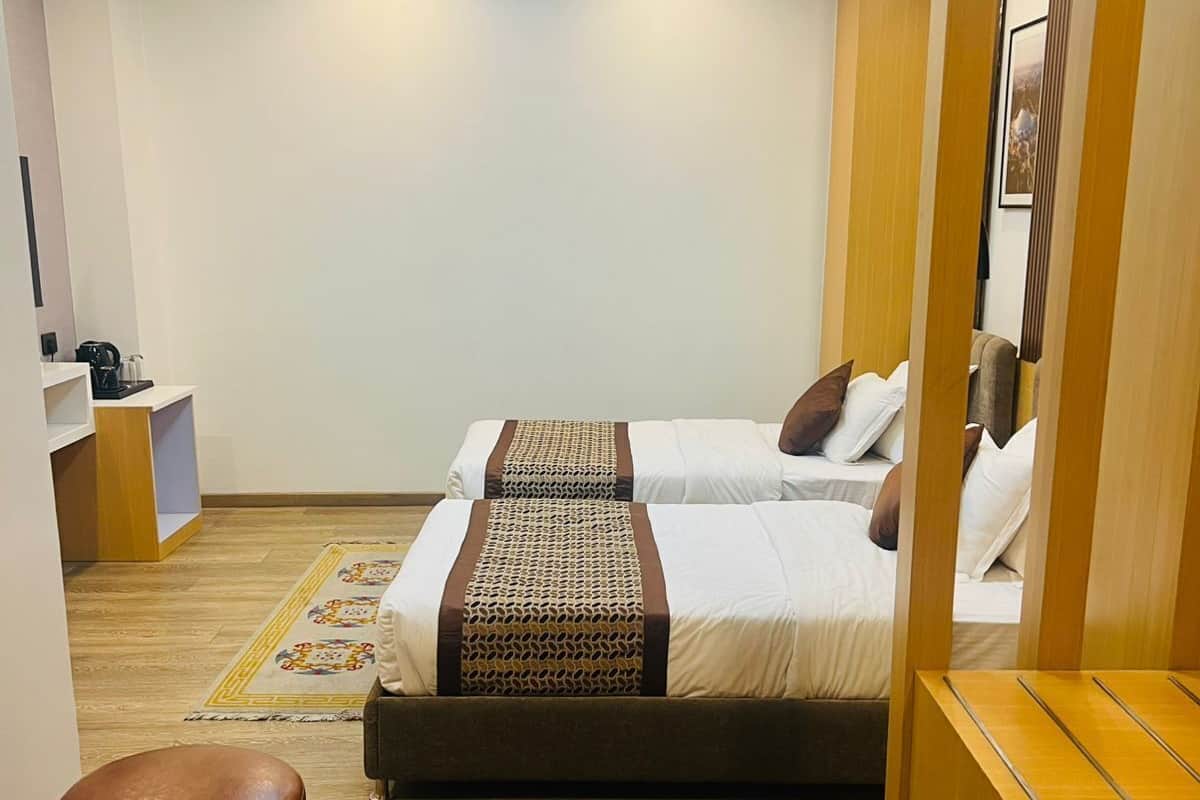 A hotel room with two beds, a wooden bench, a small table, and a desk with a menu.