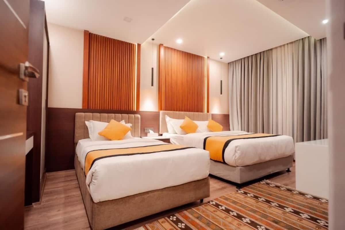 A hotel room with two beds, wooden headboards, and a patterned rug.
